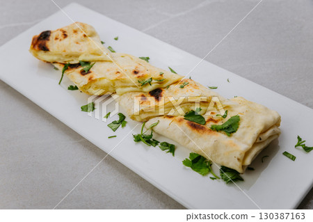 Grilled lavash rolls with melted cheese and herbs on a white ceramic plate 130387163