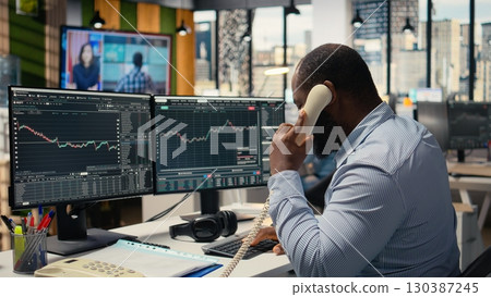 Investment consultant worried by Black Swan event causing economic loss, alerting customers. African american man watching news of stock exchange crisis doing telephone calls with clients 130387245