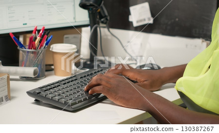 African American worker applying airway bill details and scanning labels on boxes. Package tracking, awb tags and records streamline shipping operations for large business. Camera B. 130387267