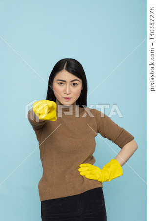 Portrait of beautiful asian woman standing in rubber gloves, pointing directly at camera with serious expression. Confident housemaid expresses confrontation and stress of housekeeping. Portrait of beautiful asian woman standing in rubber gloves, pointing directly at camera with serious expression. Confident housemaid expresses confrontation and stress of housekeeping. 130387278