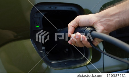Extreme close up of eco conscious driver connecting electric car to charging port, supporting transition to renewable energy transportation. Male hand inserts power connector into EV vehicle 130387281
