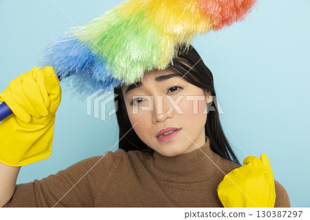 Exhausted asian female janitor touching head with feather duster, feeling overwhelmed by cleaning duties. Tired housekeeper with yellow gloves, showing signs of fatigue after long day of chores. Exhausted asian female janitor touching head with feather duster, feeling overwhelmed by cleaning duties. Tired housekeeper with yellow gloves, showing signs of fatigue after long day of chores. 130387297