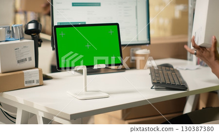 African american staff checking cardboard boxes with chroma key on computer, monitoring parcel status and shipment route via airway bill numbers on pc software. Woman in hi vis vest. Camera B. African american staff checking cardboard boxes with chroma key on computer, monitoring parcel status and shipment route via airway bill numbers on pc software. Woman in hi vis vest. Camera B. 130387380
