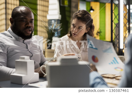 Diverse contractors real estate developers evaluating site preparation master plan and zoning regulations during a collaborative meeting. Planning session for a future housing initiative. 130387461