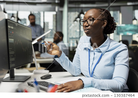 Risk analyst monitors live market activity to identify market volatility signs. African american woman reviewing portfolio performance reports, checking for potential financial risks 130387464