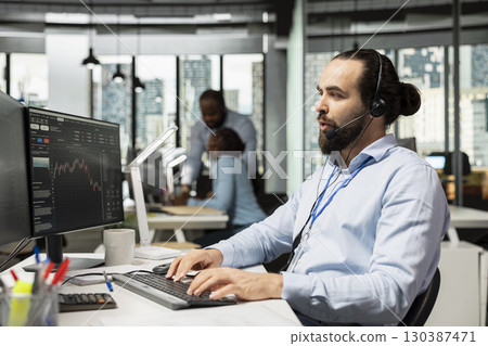 Trader working for brokerage company talking with clients, explaining stock market trends through headset mic. Man analyzing market options and recommends tailored investment strategies for customers 130387471