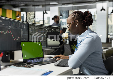 Proprietary firm employee uses green screen laptop in office to monitor live stock charts. African American woman using chroma key notebook with financial software in prop firm workspace Proprietary firm employee uses green screen laptop in office to monitor live stock charts. African American woman using chroma key notebook with financial software in prop firm workspace 130387475