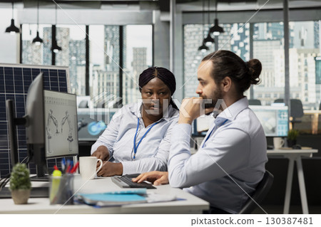 Team of engineers brainstorming solar panel cells with reduced carbon footprint designs. Teamworking colleagues in office develop robotic arm systems for automated clean energy solar panel production 130387481