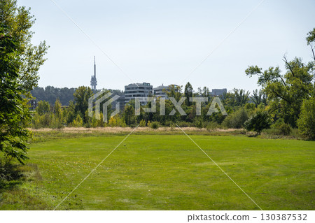 Open green grassy golf area under a clear sky with modern buildings and Zizkov TV Tower  130387532