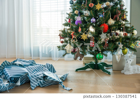 Christmas tree and excessive used gift wrap on floor - symbol of holiday consumerism and paper waste 130387541