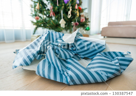 Torn Christmas wrapping paper mess near tree symbolizing holiday excess and paper overuse 130387547