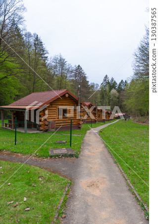Row of cozy wooden cabins with red roofs in spring forest retreat, paved path and fenced yards 130387565