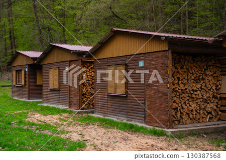 Wooden cabins with shuttered windows, stacked firewood in forest, traditional rural architecture 130387568