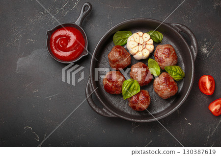 Delicious fried meatballs with basil, garlic in cast iron pan and tomato sauce top view, copy space 130387619