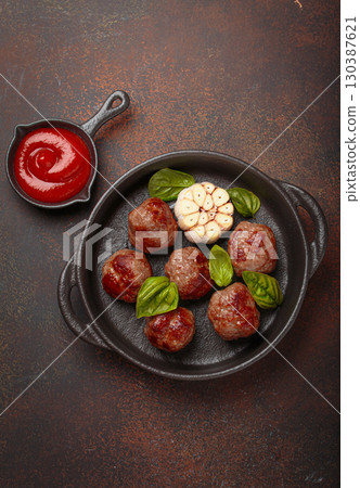 Delicious fried meatballs with basil, garlic in cast iron pan and tomato sauce top view 130387621