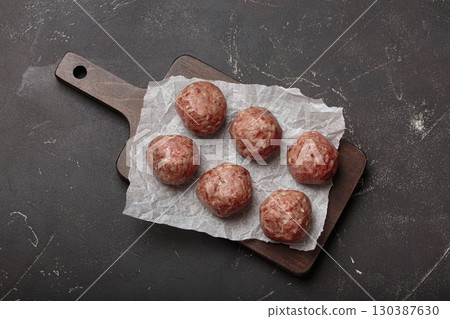 Raw meatballs sitting on wooden cutting board with parchment paper Raw meatballs sitting on wooden cutting board with parchment paper 130387630