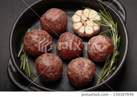 Raw meatballs with rosemary and garlic in black cast iron pan on rustic black background Raw meatballs with rosemary and garlic in black cast iron pan on rustic black background 130387646