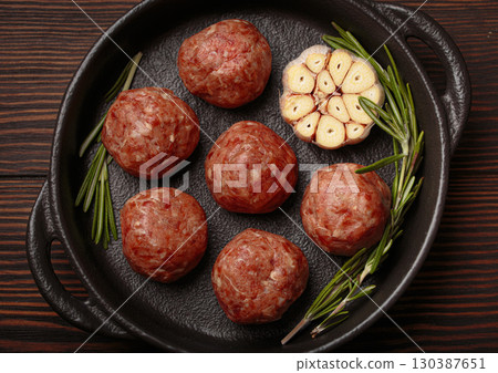 Raw meatballs with garlic and rosemary in cast iron pan on wooden background 130387651