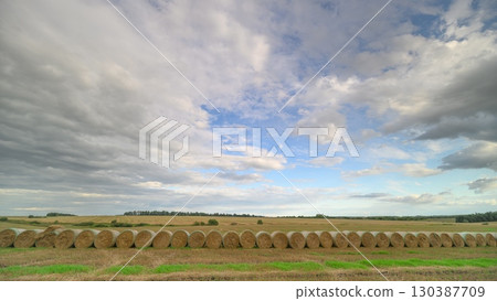 A beautiful and scenic rural landscape featuring hay bales beneath a cloudy sky above 130387709