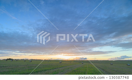 A Beautiful Sunrise Spreading Over Expansive Fields Complemented by Dramatic Clouds 130387748