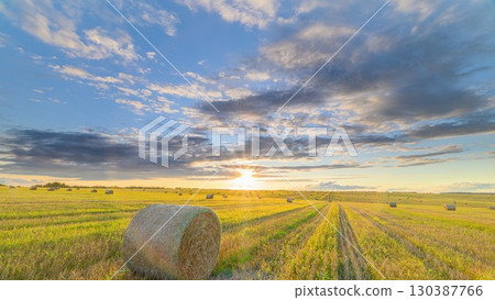 A breathtaking and scenic sunset over rolling fields adorned with golden bales of hay 130387766