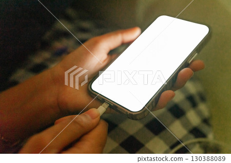 A person is plugging in their phone while seated on a checkered blanket outdoors A person is plugging in their phone while seated on a checkered blanket outdoors 130388089