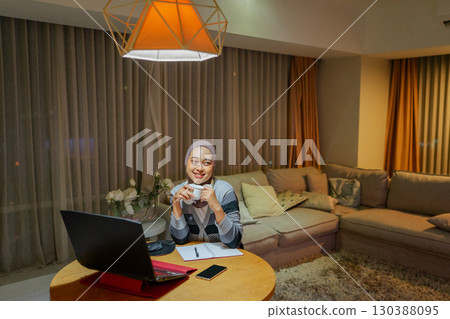 A young woman is working from home in a cozy, creative living room with her laptop 130388095