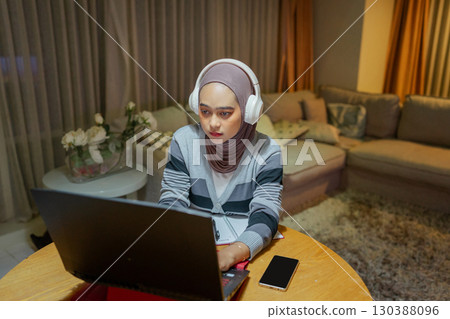 A Focused Young Woman Diligently Working on Her Laptop in a Cozy Living Room Space 130388096