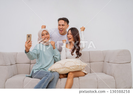 A group of friends happily taking a selfie together on their couch with a smartphone A group of friends happily taking a selfie together on their couch with a smartphone 130388258