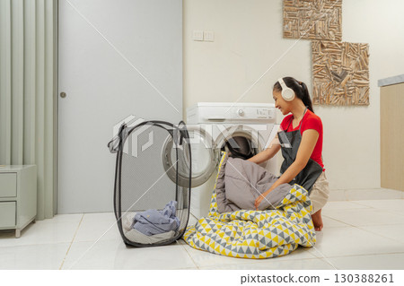 Woman Handling Laundry at Home with Headphones and Relaxing Atmosphere 130388261