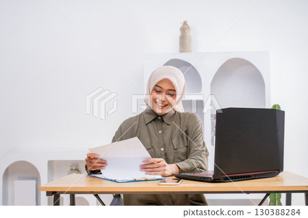 Young Woman Working Remotely with Papers and Laptop in Cozy Home Office 130388284