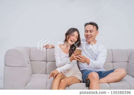 A Happy Couple Sitting Together on a Comfortable Couch with Smartphone Enjoying Time A Happy Couple Sitting Together on a Comfortable Couch with Smartphone Enjoying Time 130388396