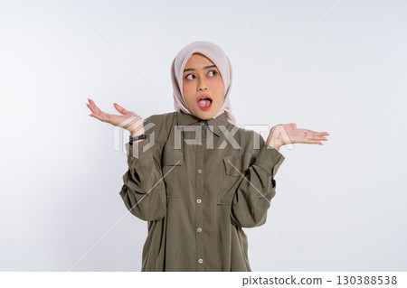 A Young Woman Wearing a Hijab is Expressing Her Surprise with Her Hands Raised Up 130388538