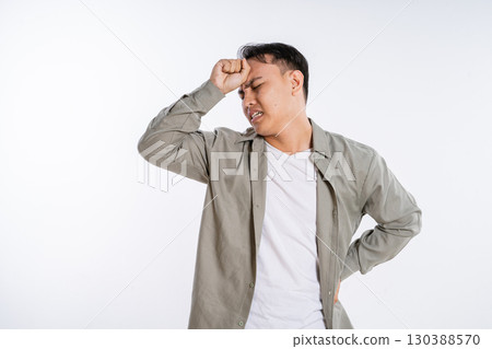 A Frustrated Young Man Holding His Head in Pain and Discomfort While Standing 130388570