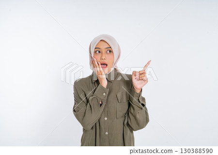 Surprised Woman in Hijab Pointing with Shocked Expression on White Background 130388590