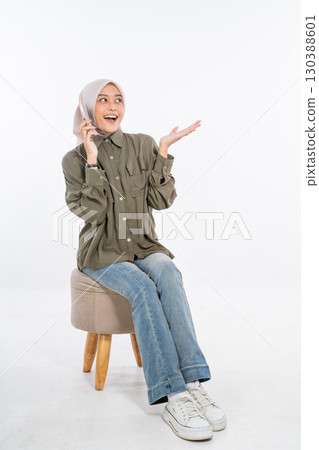 A Cheerful Young Woman Engaged in a Phone Conversation While Sitting on a Stool 130388601