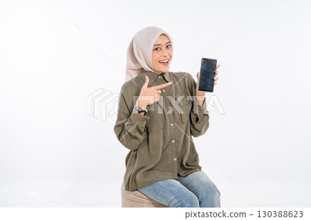 A Cheerful Woman is Cheerfully Displaying a Smartphone on a Bright White Background 130388623