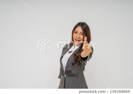 A successful businesswoman is proudly giving a thumbs up in professional attire A successful businesswoman is proudly giving a thumbs up in professional attire 130388669