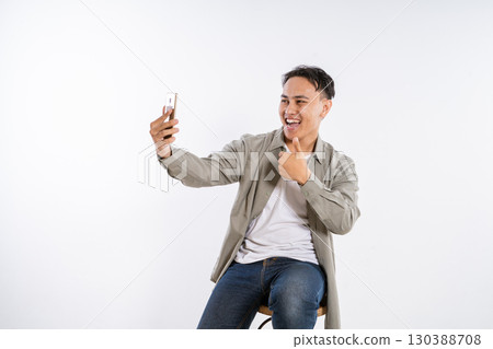 Cheerful Young Man Taking a Selfie with a Smartphone in a Studio Setting Cheerful Young Man Taking a Selfie with a Smartphone in a Studio Setting 130388708