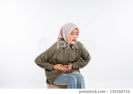 Young Woman with Abdominal Pain Sitting on a Stool in a Studio Setting 130388710