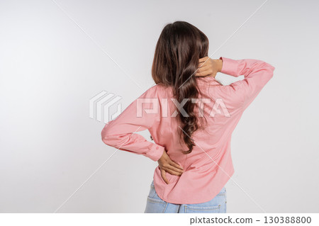 A Woman Experiencing Back Pain While Stretching in a Casual Pink Shirt, Captured Candidly 130388800