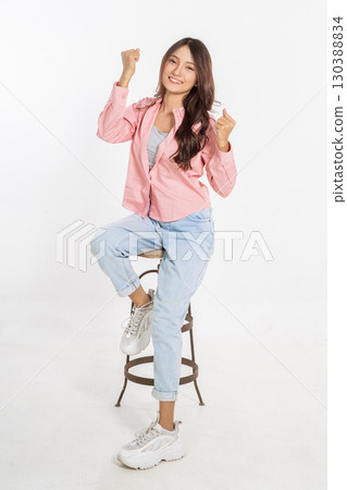 A Joyful Young Woman is Celebrating on a Stool, Radiating a Bright Smile of Happiness 130388834
