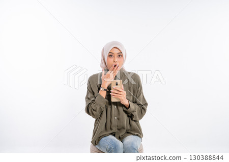 A young woman in a studio holds a smartphone, expressing joy and excitement A young woman in a studio holds a smartphone, expressing joy and excitement 130388844