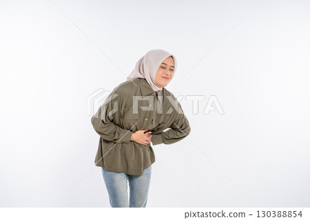 A young woman wearing a hijab is currently experiencing some stomach discomfort A young woman wearing a hijab is currently experiencing some stomach discomfort 130388854