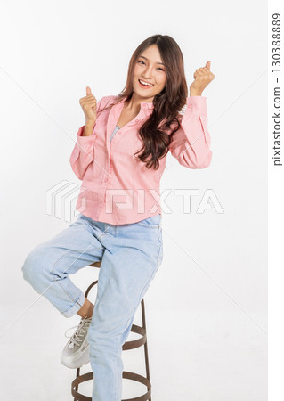 A Cheerful Young Woman is Posing on a Stool while Making a Playful Gesture, radiating joy A Cheerful Young Woman is Posing on a Stool while Making a Playful Gesture, radiating joy 130388889
