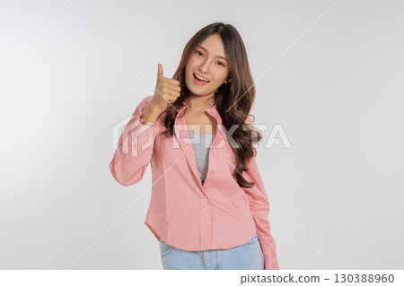 A cheerful young woman gives a thumbs up gesture while dressed in a stylish outfit, A cheerful young woman gives a thumbs up gesture while dressed in a stylish outfit, 130388960