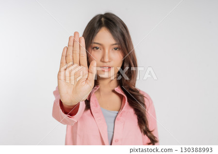 A Young Woman is Gesturing Stop with Her Outstretched Hand in a Studio Setting 130388993
