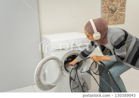 A woman wearing headphones is doing laundry in a contemporary home setting 130389043