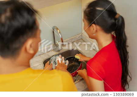 A couple collaborating together on dishwashing in a contemporary kitchen setting A couple collaborating together on dishwashing in a contemporary kitchen setting 130389069