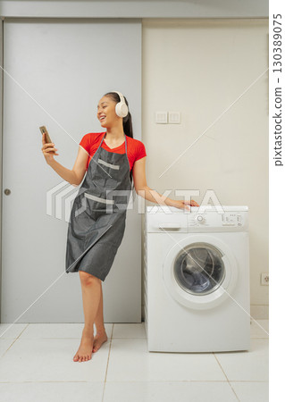 A woman is joyfully enjoying music while she multitasks and does laundry at home A woman is joyfully enjoying music while she multitasks and does laundry at home 130389075